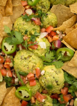 A platter of scoops of guacamole with pico de gallo and tortilla chips.