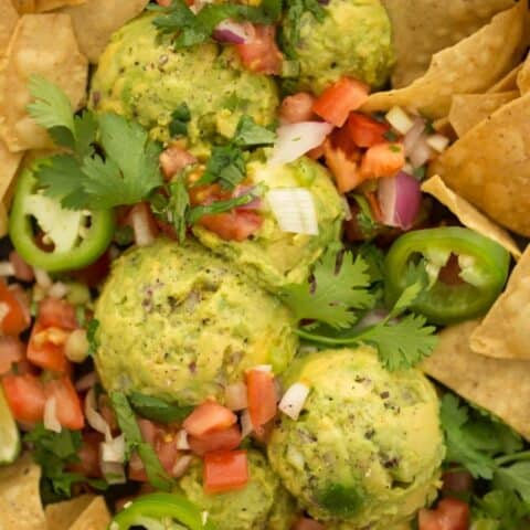 A platter of scoops of guacamole with pico de gallo and tortilla chips.