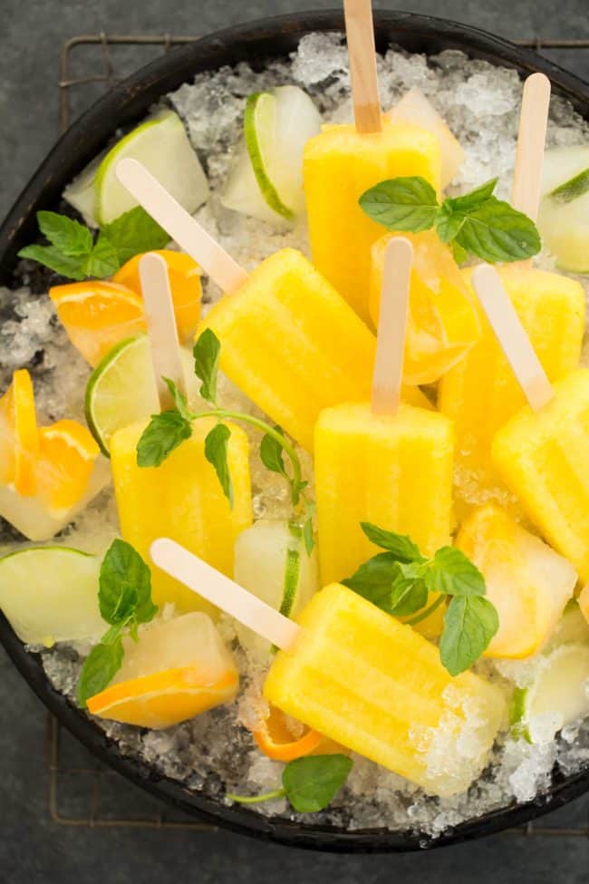 A black tray filled with crushed ice and Pineapple paletas. 