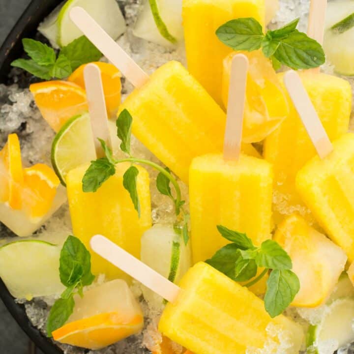 A round black tray filled with crushed ice and pineapple Mexican paletas.