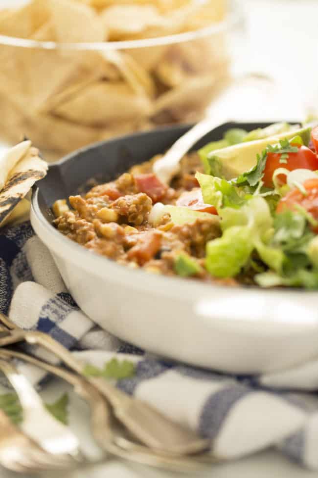skillet filled with ground turkey and refried beans topped with cherry tomatoes and avocado