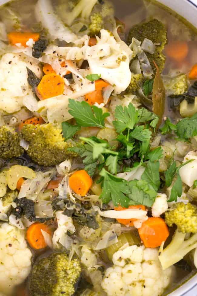 A white pot filled with hearty vegetable soup with cabbage.