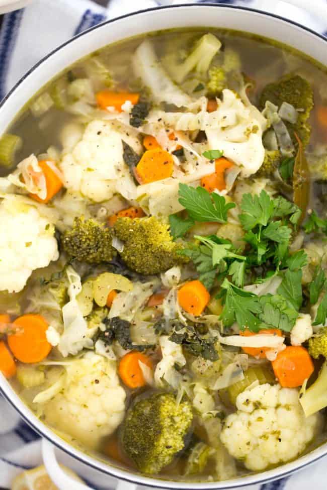 A white pot filled with vegetable soup with cabbage.