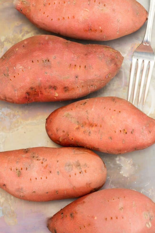 Five root vegetables on a cookie sheet with a fork next to then.