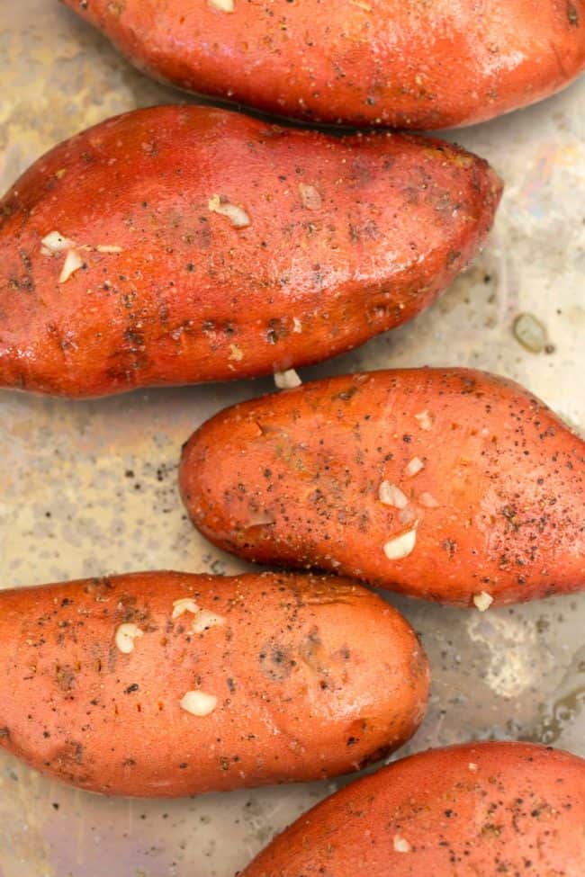 cookie sheet with sweet potatoes rubbed with olive oil and garlic for baking