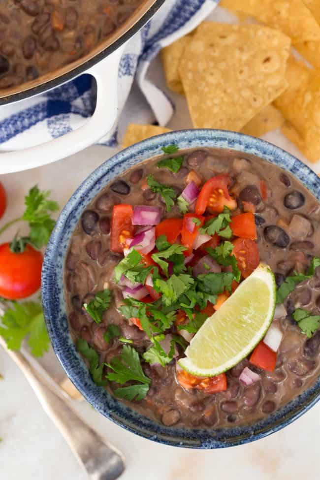 A blue bowl filled with Creamy Black Beans with Coconut Milk garnished with pico de gallo.