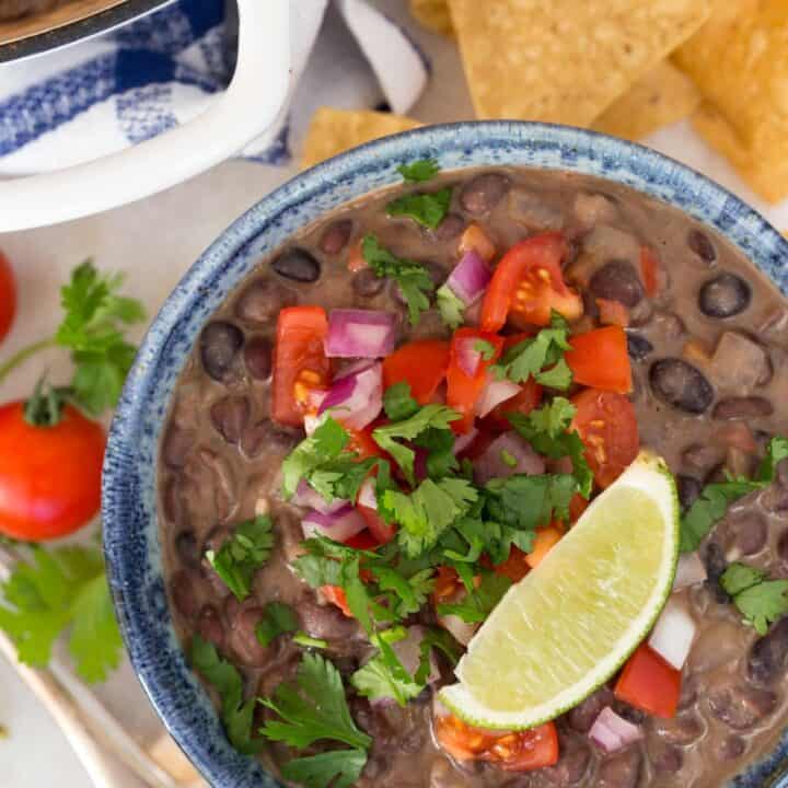 A blue bowl filled with Creamy Black Beans with Coconut Milk garnished with pico de gallo.