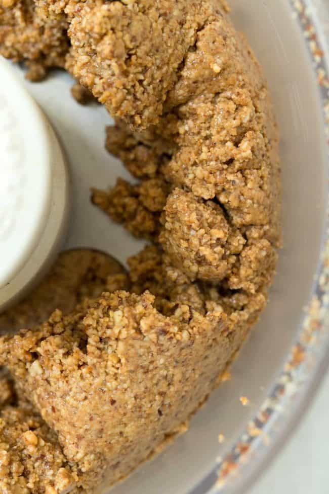 A food processor bowl filled with ground almonds for almond butter.