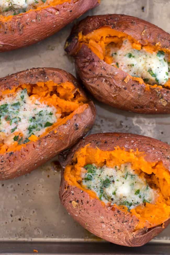 A cooking sheet filled with baked sweet potatoes with melted herbed butter