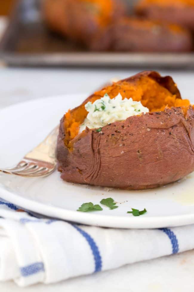 A baked sweet potato stuffed with melting herbed butter on a plate.