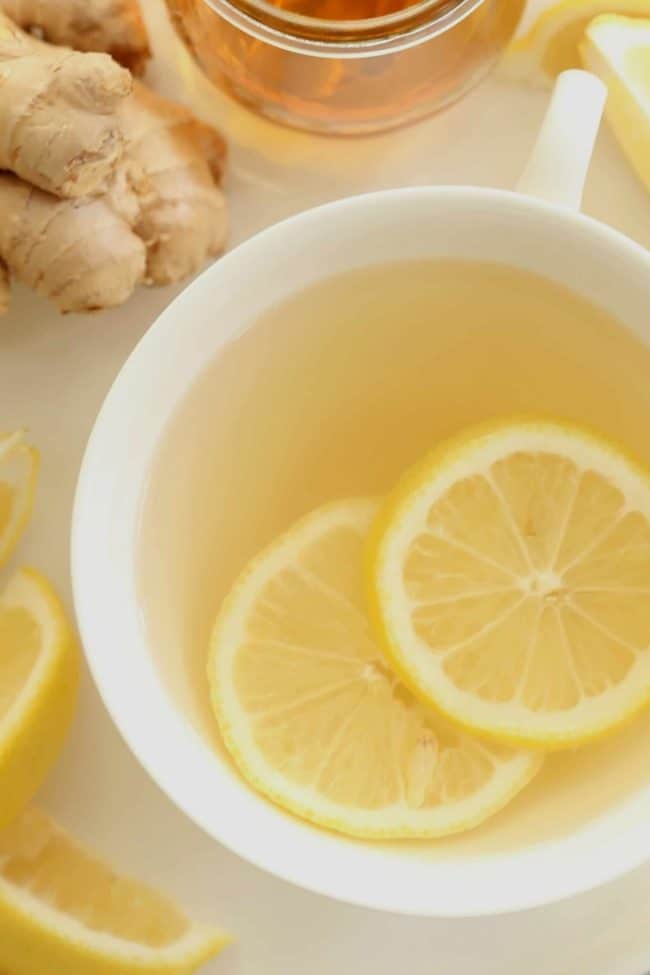 A white tea cup filled with ginger tea for cold and lemon slices.