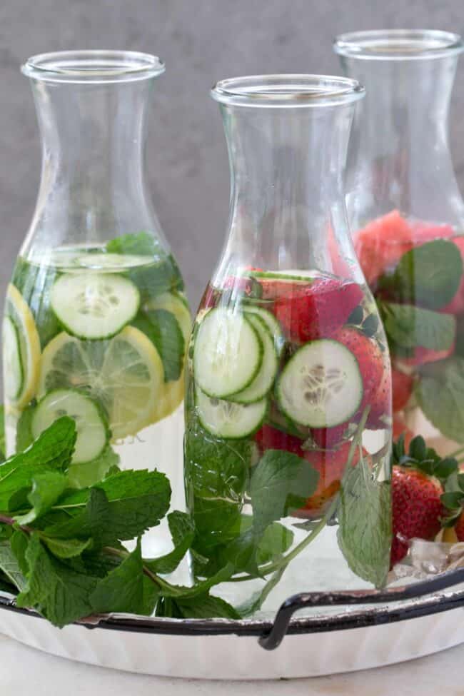 Three clear jars filled with H2O and slices of cucumber, lemons and strawberries.