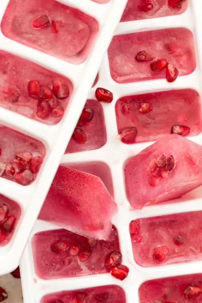 Two white ice cube trays filled with frozen pomegranate water ice cubes.