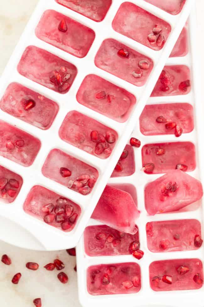 Two white ice cube trays filled with frozen fruit and water.