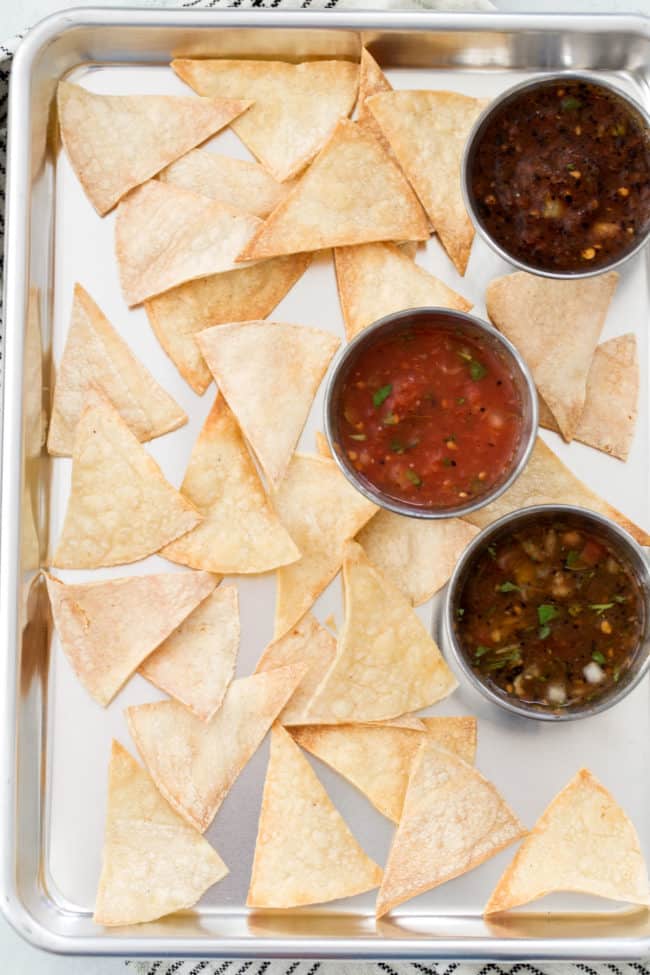 A cookie sheet filled with baked chips and 3 types of salsa.