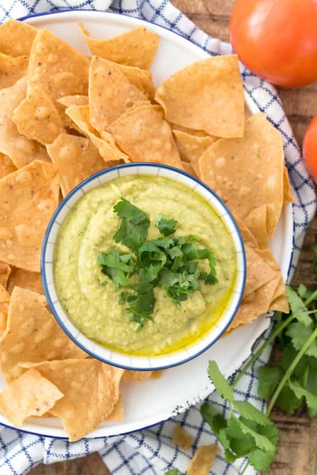 A bowl of jalapeno hummus on a plate filled with tortilla chips.