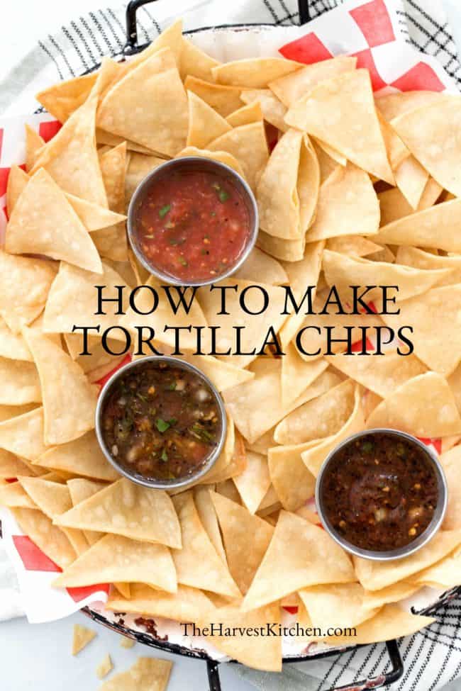 A platter filled with homemade tortilla chips and 3 containers of salsa.