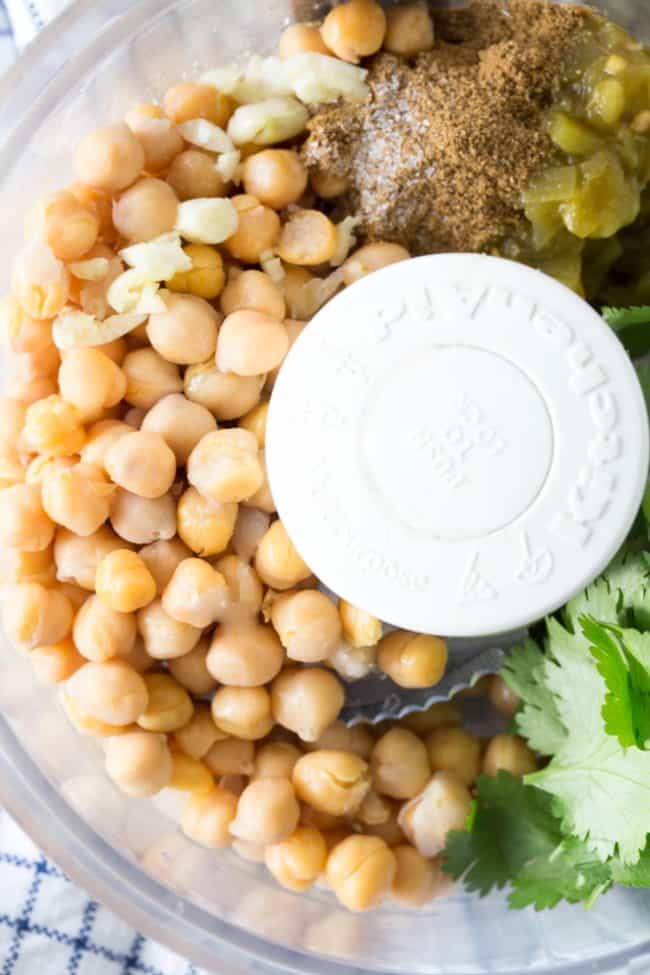 A food processor filled with chickpeas and spices and fresh cilantro.