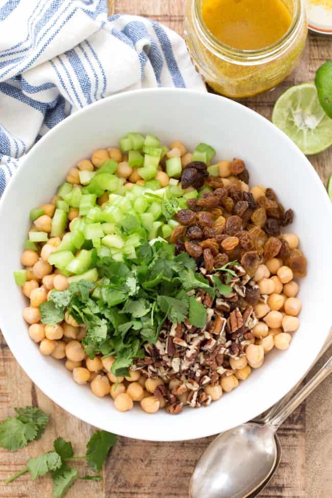 white bowl with garbanzo beans, chopped celery, cilantro, raisins and pecans