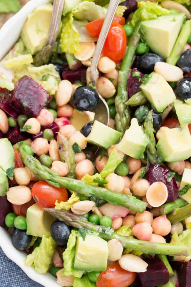 White bowl with tossed house salad of romaine lettuce, chopped beets, peas, asparagus and avocado.