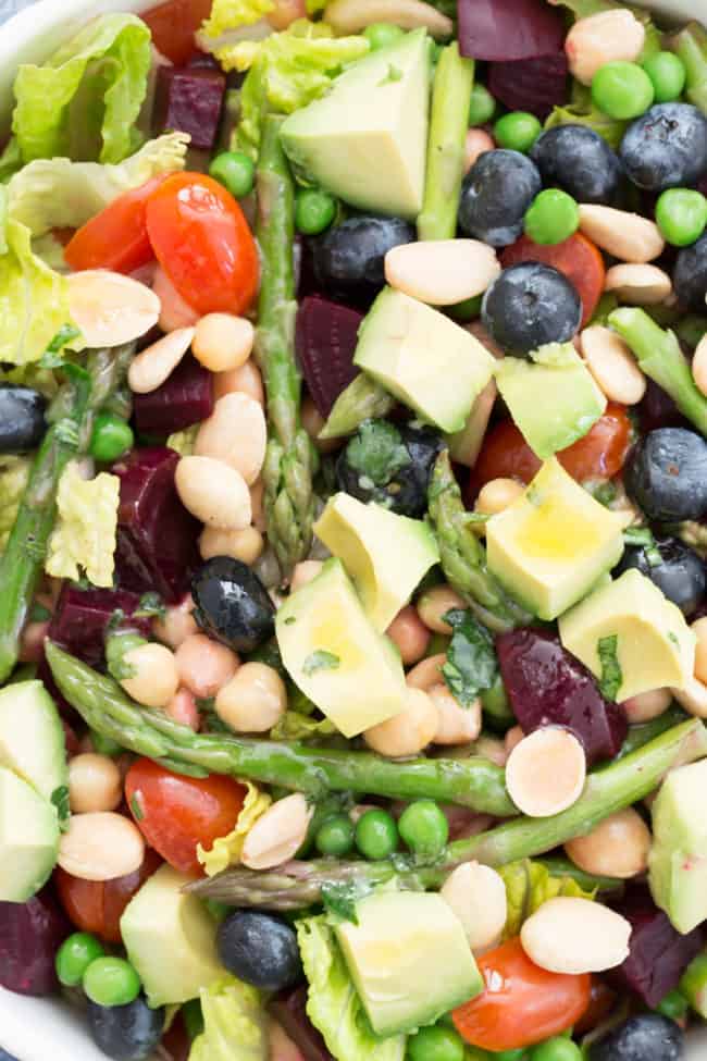 White bowl with tossed house salad of romaine lettuce, chopped beets, peas, asparagus and avocado.