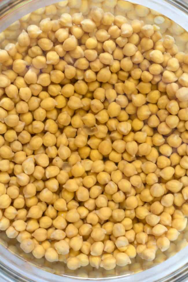 A clear glass bowl filled with legumes soaking in water.