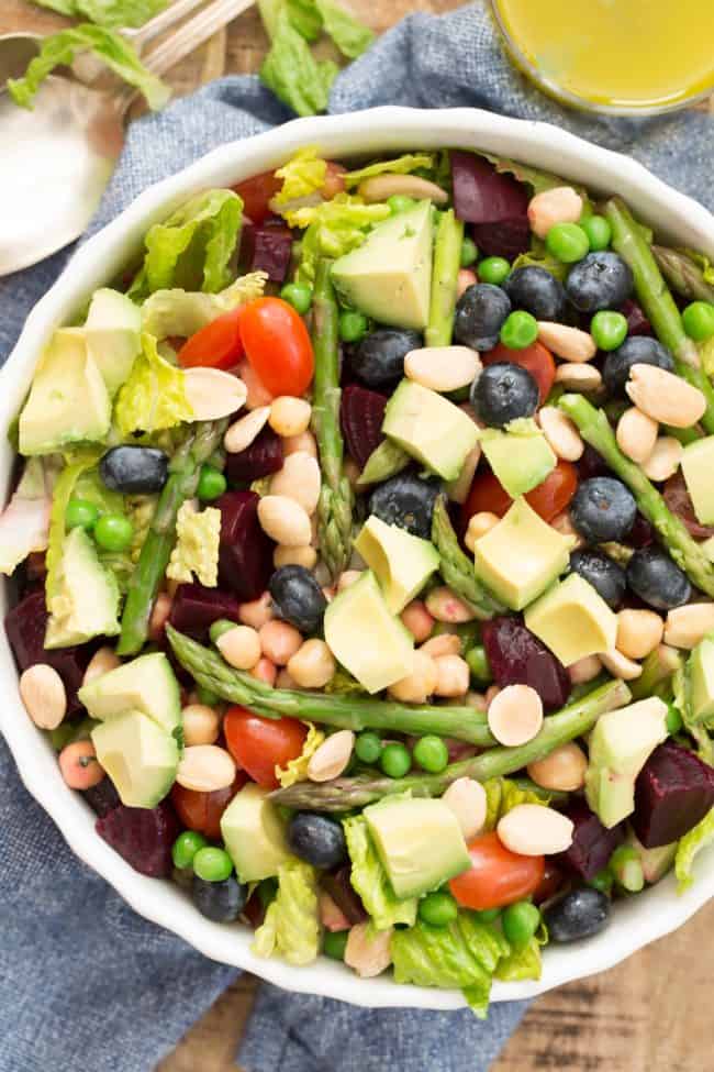 White bowl with romaine lettuce, chopped beets, peas, asparagus and avocado.