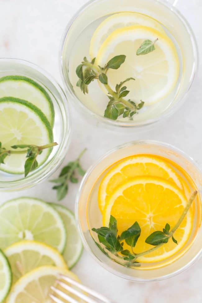 Two clear glasses filled with oregano tea and citrus slices.