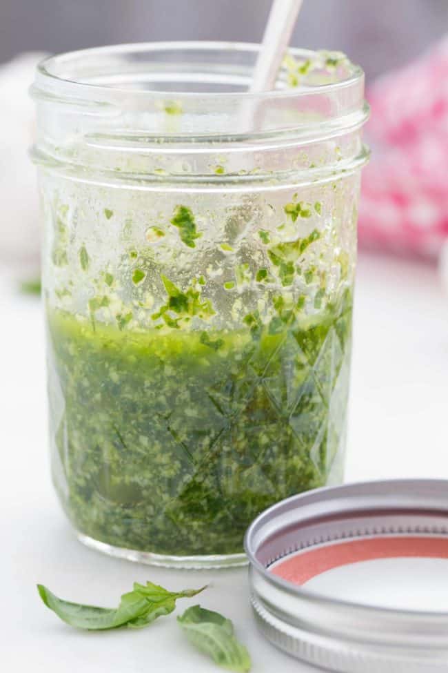 A clear glass jar filled with homemade basil pesto.