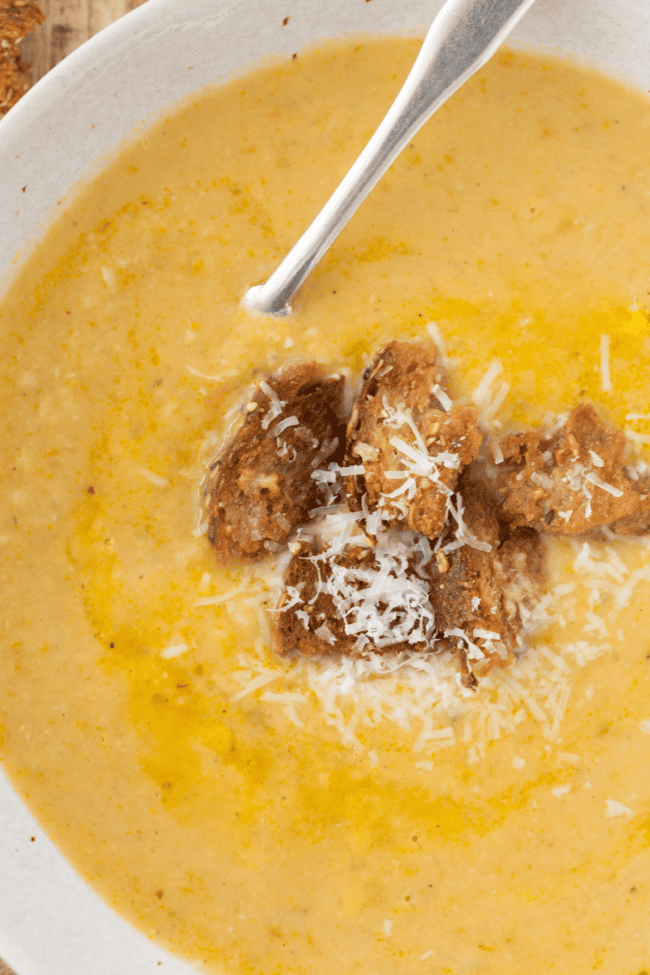 A white bowl filled with creamy white bean soup. Croutons rest on top of the soup.