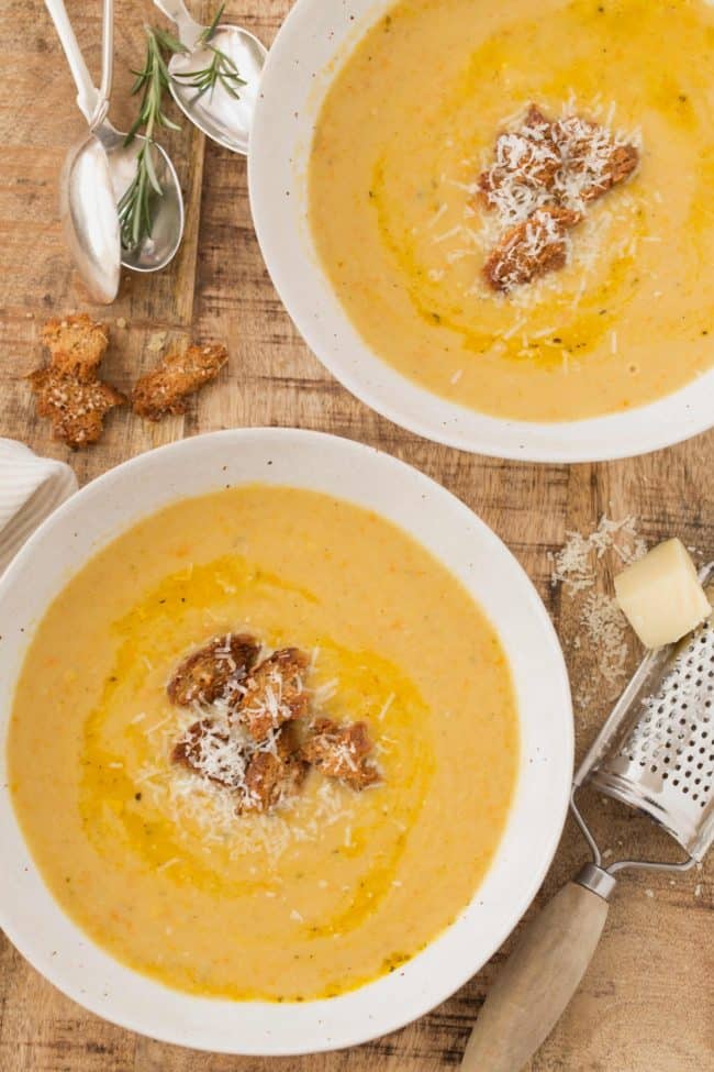 Two white bowls filled with Vegetarian Bean Soup. A cheese grated with a wedge of Parmesan cheese sits next to the bowls. 