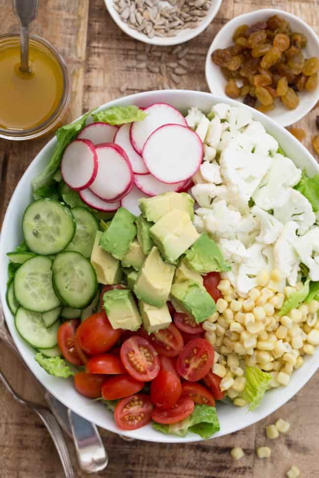 A large white bowl filled with lettuce, sliced cucumber, tomatoes, avocado and radishes.