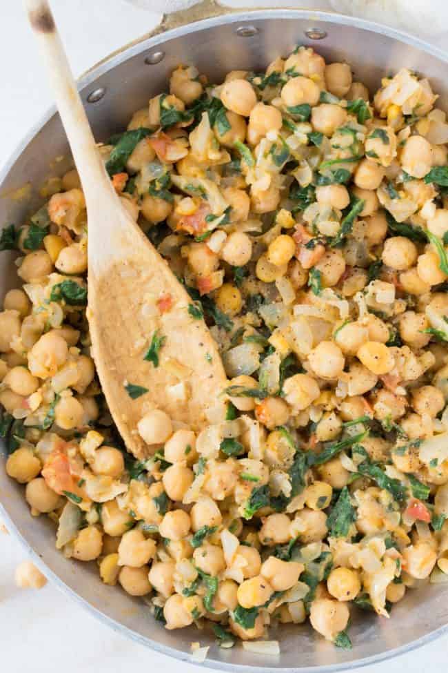 An aluminum skillet with wooden spoon and cooked chickpeas and spinach.