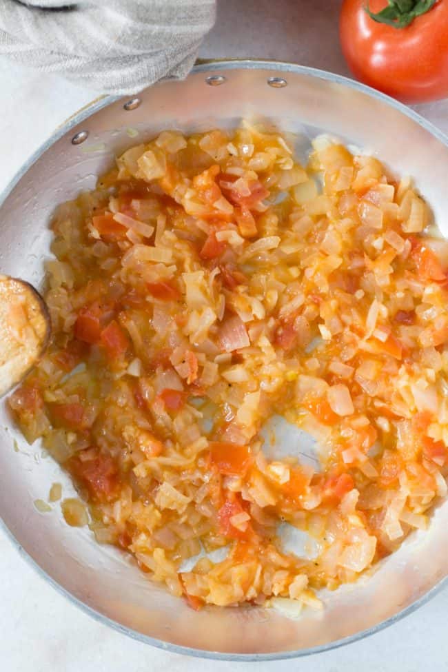 An aluminum skillet of cooked onions and tomatoes.