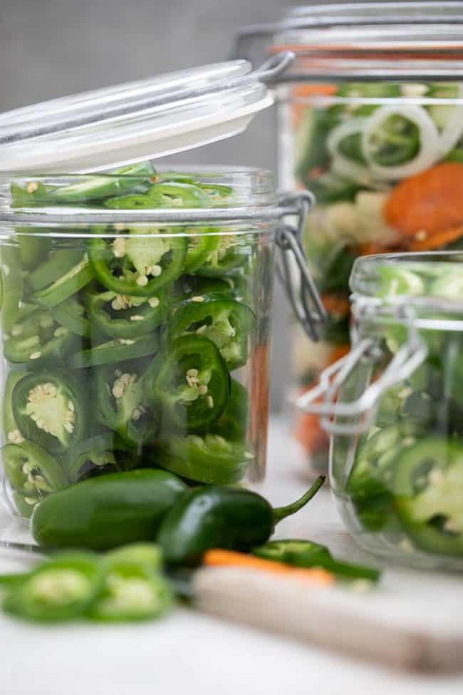 Three clear glass mason jars filled with sliced peppers. A knife sits next to the jars.