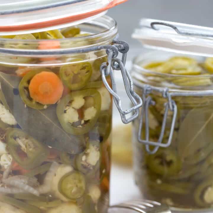 Two clear glass mason jars filled with pickled jalapenos.
