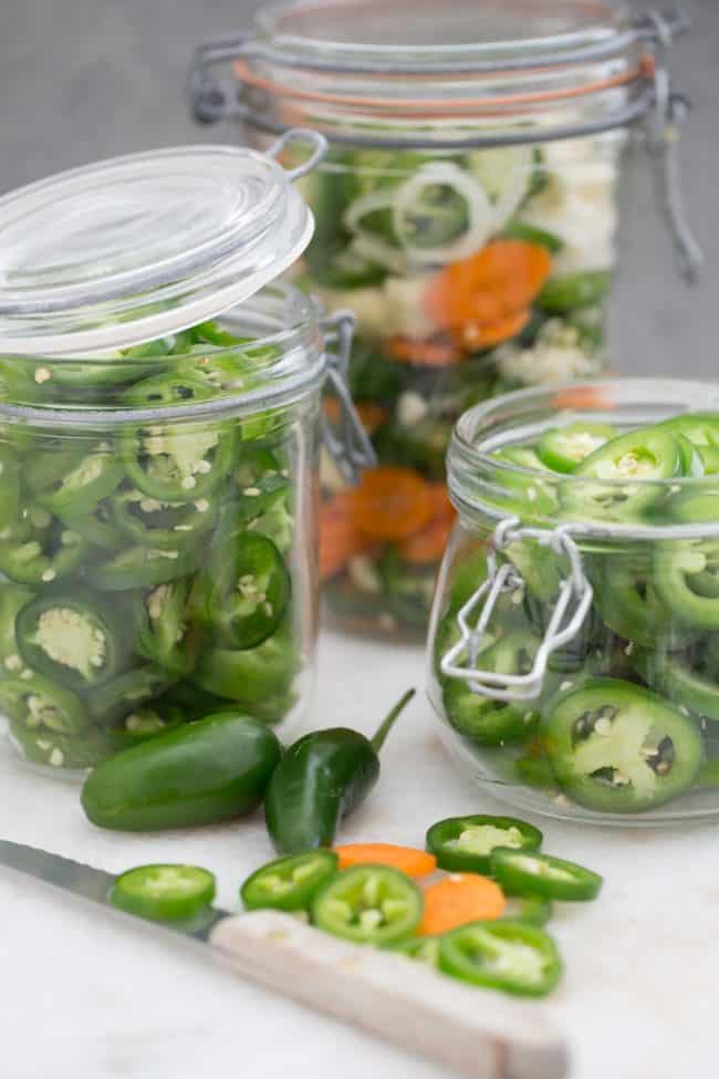 Three mason jars filled with sliced peppers. A knife sits next to the jars.