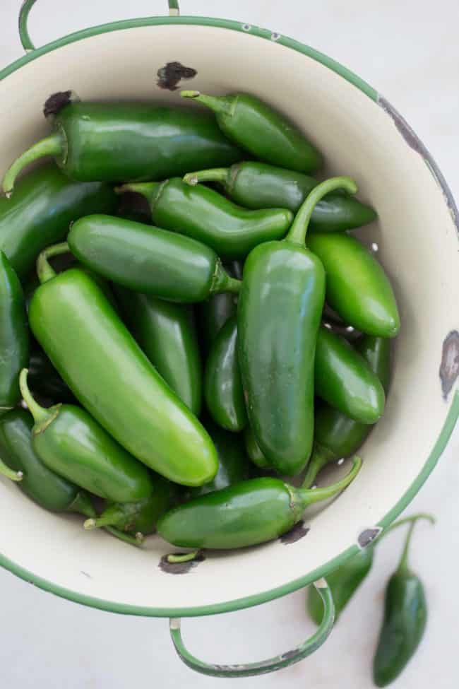 A white colander with a green trim filled with raw green peppers.