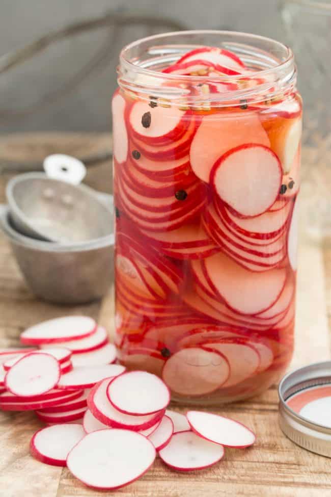 A clear glass mason jar of quick pickled radishes.