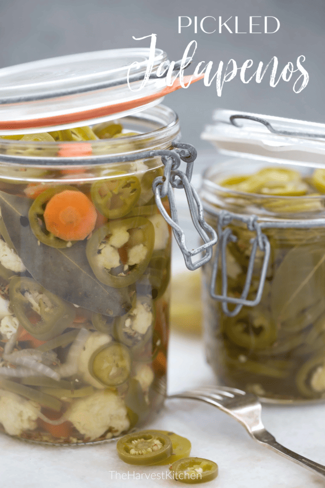 Two clear glass mason jars filled with pickled jalapeno peppers.