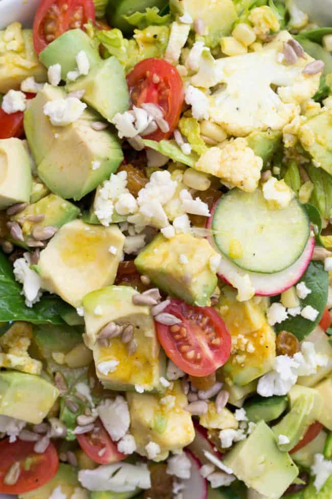 A bowl of filled with lettuce, chopped avocado, sliced cucumber, radishes and tomatoes.