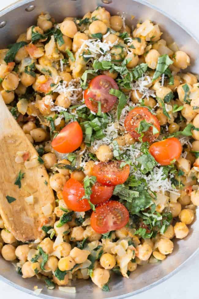 An aluminum skillet with cooked chickpeas and spinach with fresh basil and cherry tomatoes.