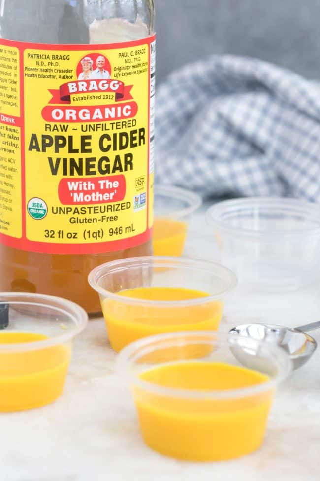 Three small plastic cups filled with ground root and apple cider vinegar. A bottle of Bragg apple cider vinegar sits next to the plastic cups.