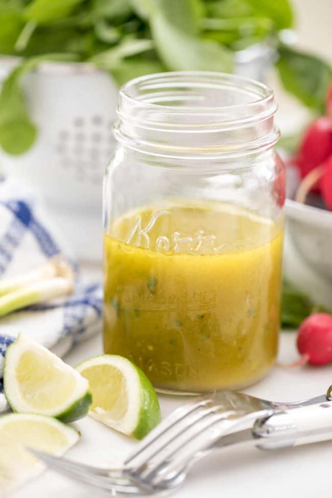 A glass mason jar half filled with homemade salad dressing. Colander in the back with lettuce.