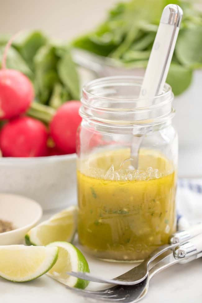 A glass mason jar half filled with homemade salad dressing. Colander in the back with lettuce.
