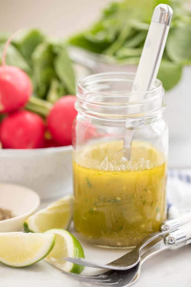 glass mason jar half filled with homemade salad dressing. Colander in the back with lettuce.