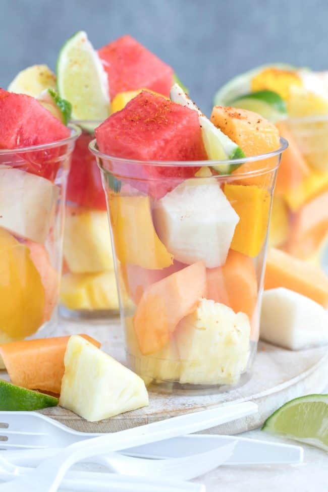 Clear plastic drinking glasses filled with watermelon and pineapple.