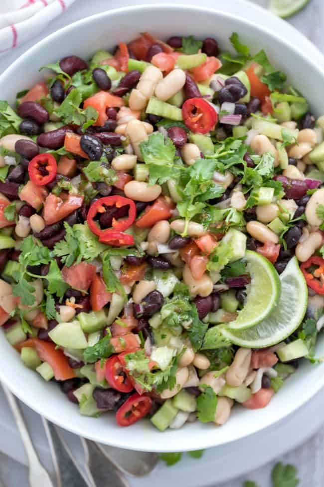 A white bowl filled with three bean salad. Red and white dish towel next to the bowl with a serving spoon.