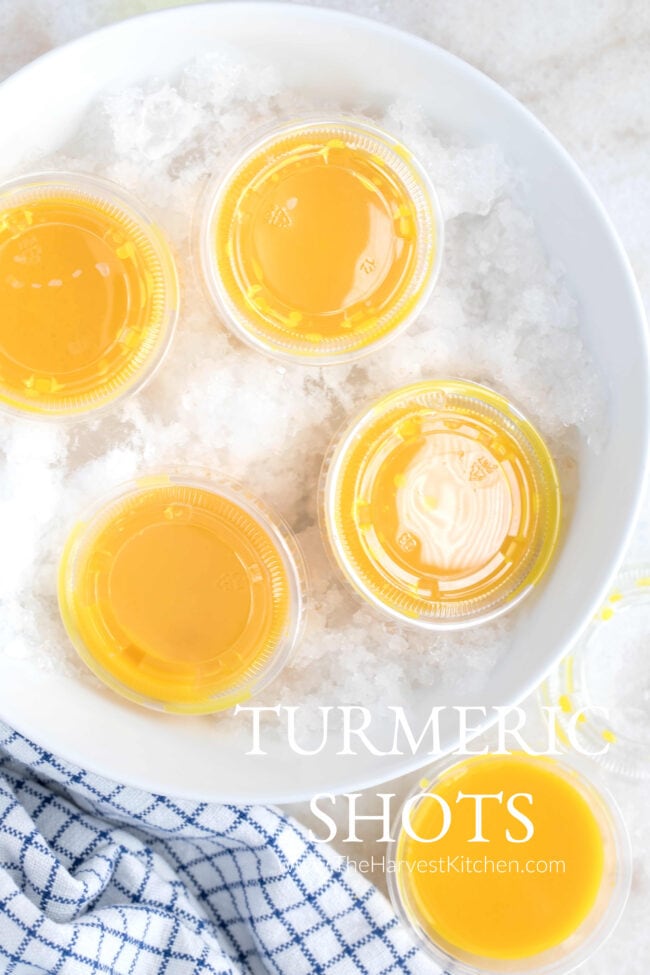 Five little cups of lemon ginger turmeric shots. Four of the little cups sit in a white bowl filled with crushed ice.