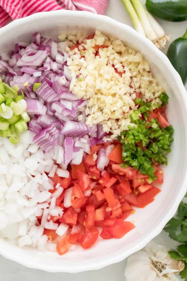 A white bowl filled with chopped tomato, onion, green onion, garlic and cilantro.